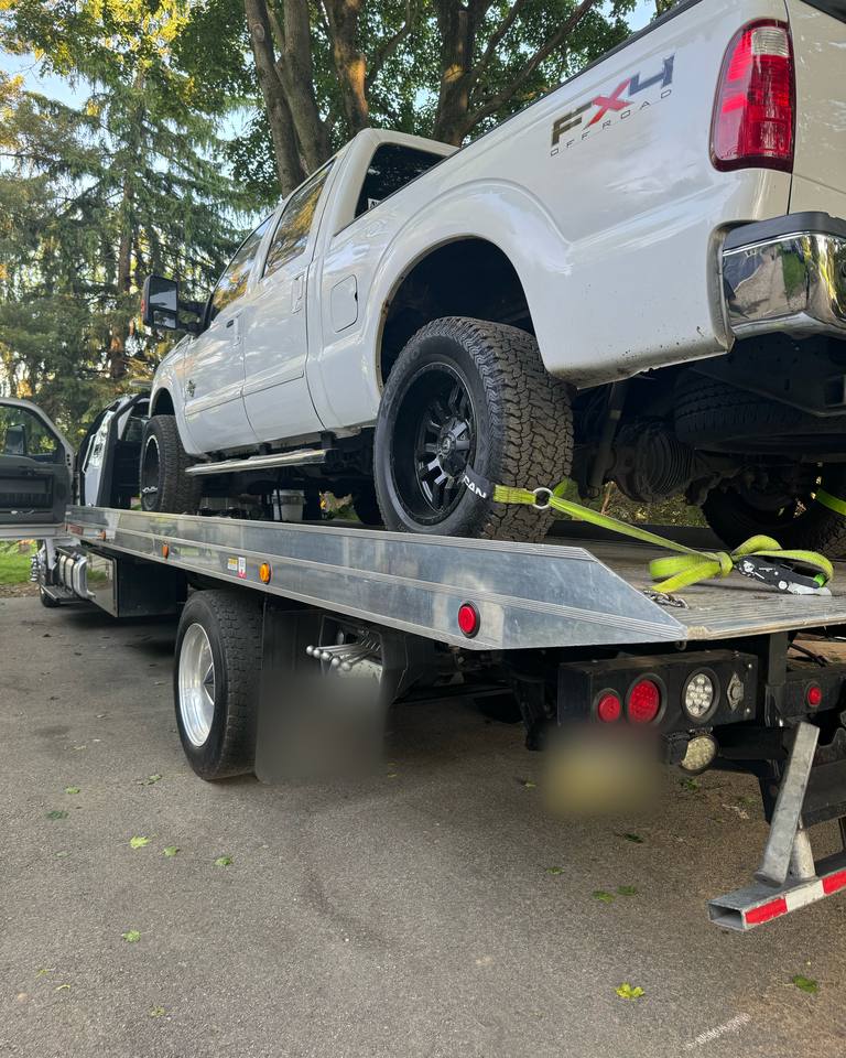 White Ford F-250 pickup truck secured with tie-down straps on a flatbed tow truck
