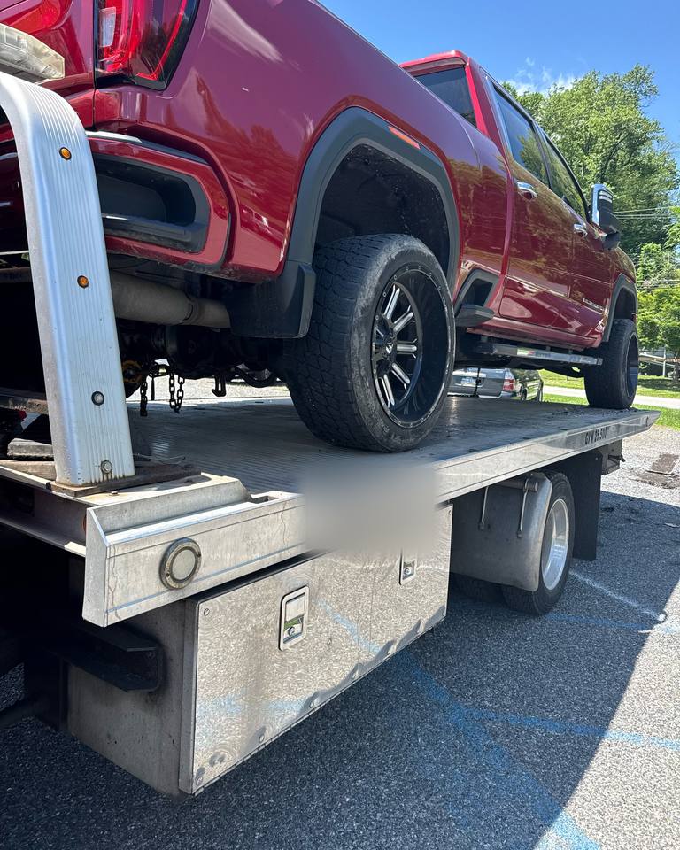 Red GMC pickup truck strapped down on the bed of a flatbed tow truck